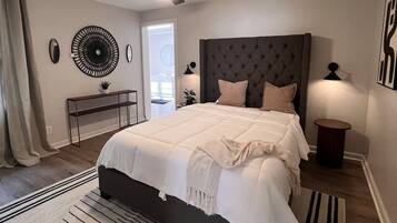 Ein Schlafzimmer mit einem Bett, einem Deckenventilator, einem Nachttisch, einer Lampe und Blick ins Freie.