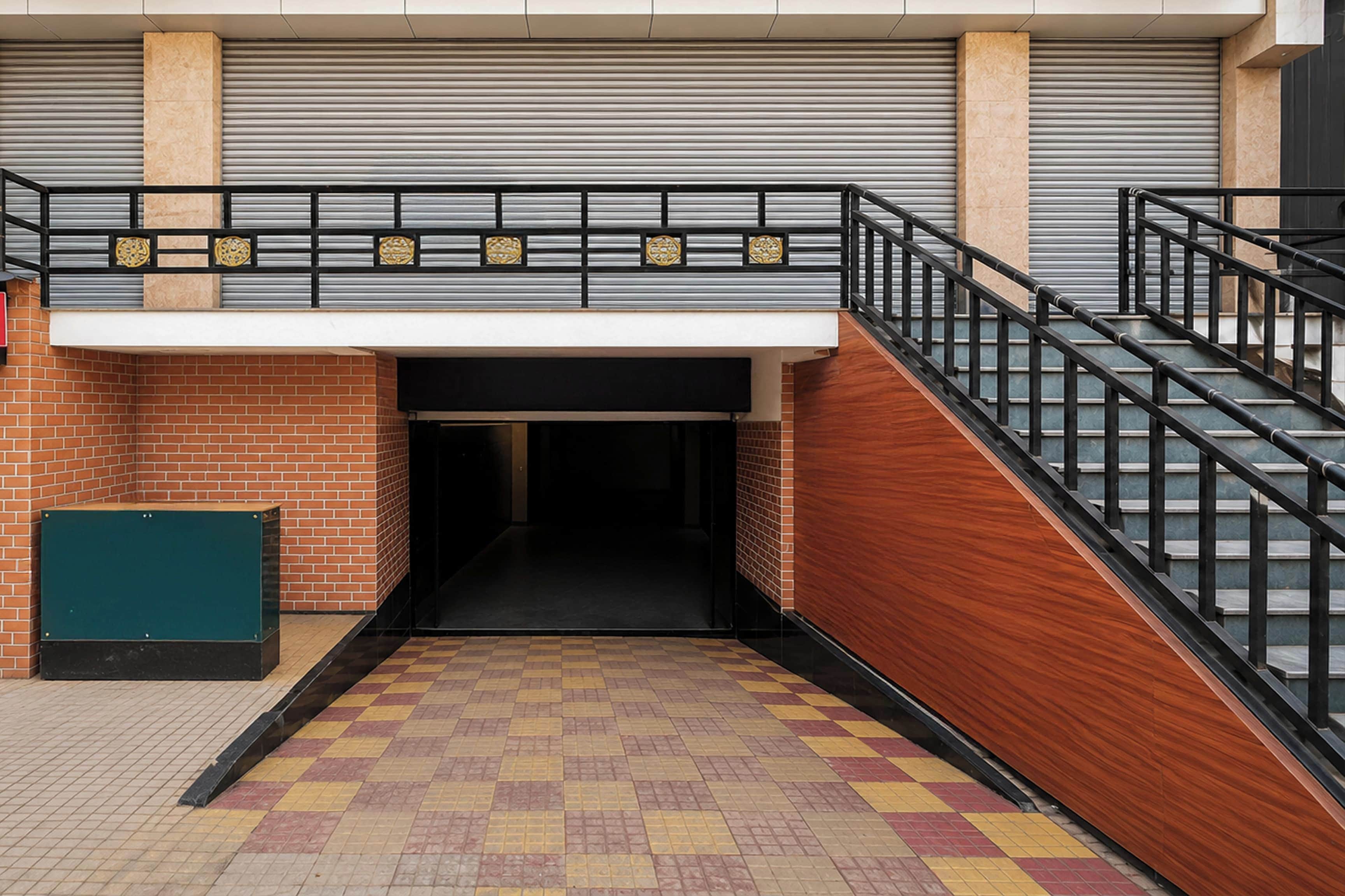 Une entrée d’immeuble avec un mur en briques, un portail en métal et un escalier doté d’une rampe noire.