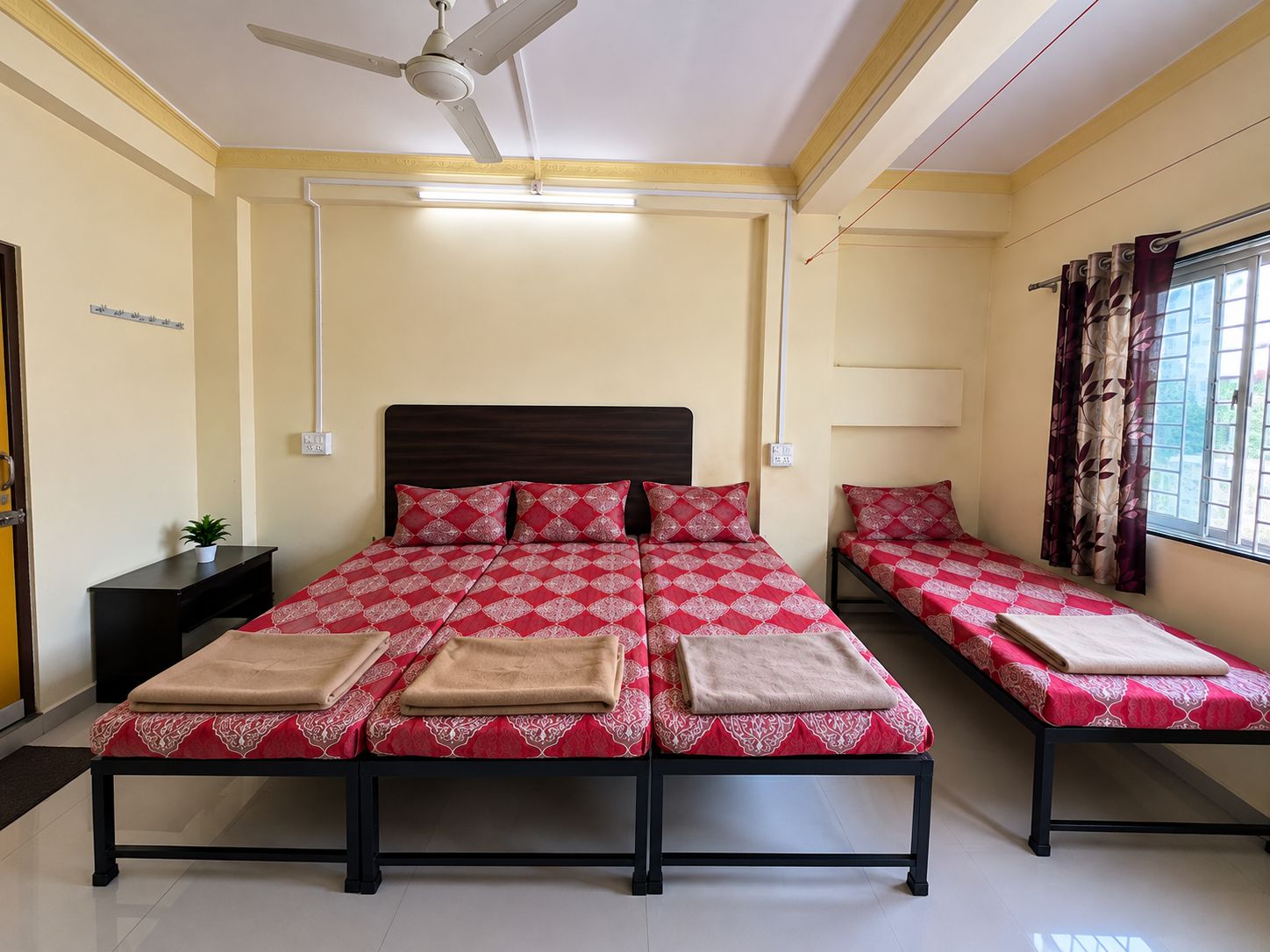 Una habitación de hotel con una cama grande, dos mesitas de noche, un ventilador de techo y una ventana con cortinas.