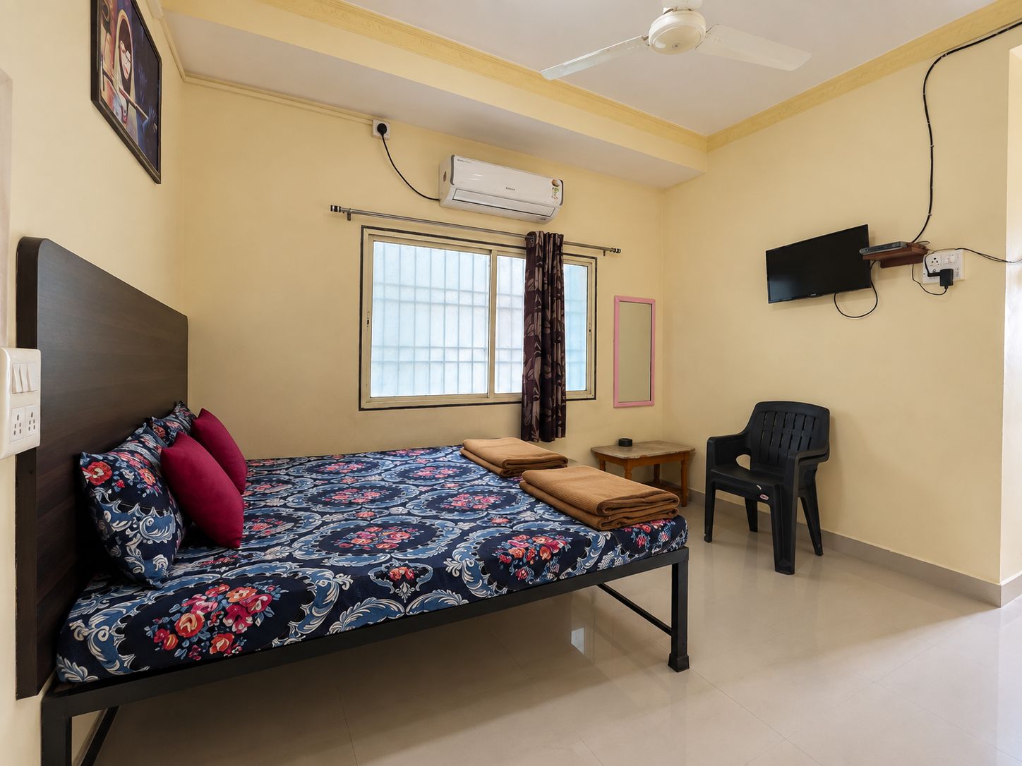 Una habitación con cama, escritorio, silla, televisor y aire acondicionado.