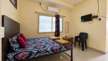 Una habitación con cama, escritorio, silla, televisor y aire acondicionado.