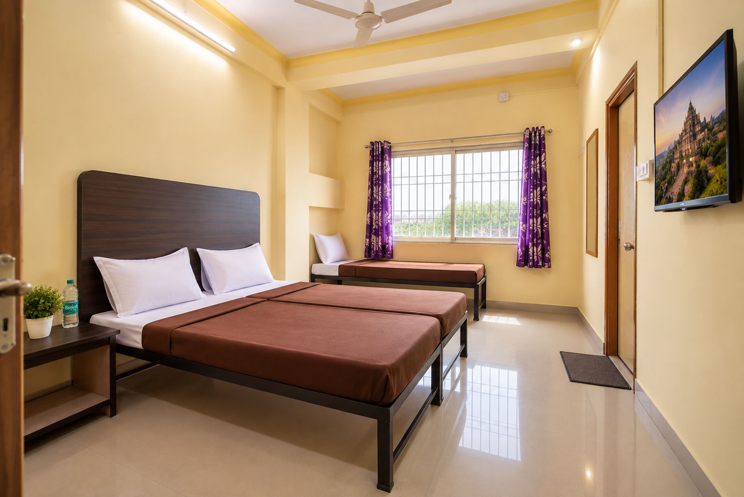 A hotel room with a bed, bedside tables, a chair, a window with curtains, and a television.