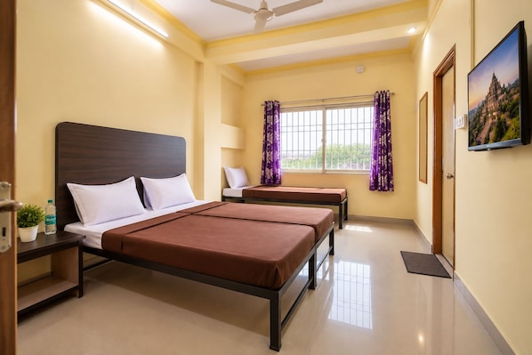 Habitación de hotel con cama, mesitas de noche, una silla, ventana con cortinas y televisor.