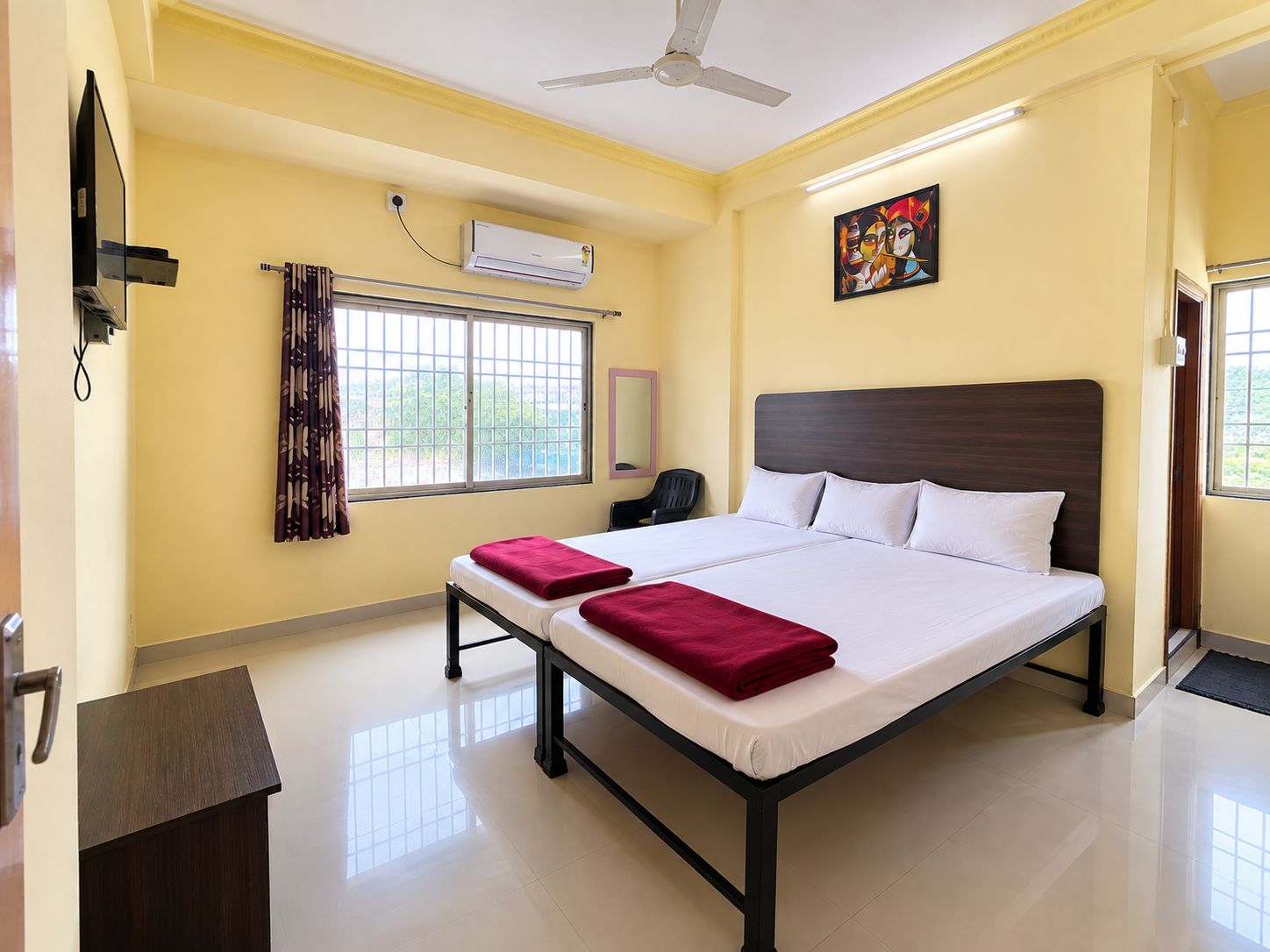 A hotel room with a bed, a desk, a chair, an air conditioning unit, a ceiling fan, and a window with curtains.