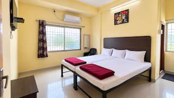 A hotel room with a bed, a desk, a chair, an air conditioning unit, a ceiling fan, and a window with curtains.