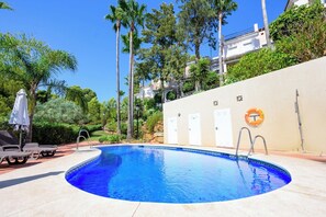 A swimming pool with a curved edge, surrounded by lounge chairs and umbrellas, with a lifebuoy and a door on the adjacent wall. - Villa INTMA Golf – Your Retreat in the Heart of Nature  (AN)