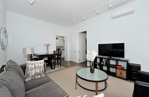 Een moderne woonkamer met een bank, een salontafel, een flatscreen televisie en een eethoek met een tafel en stoelen.
