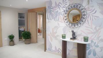 A hallway with a mirror, potted plants, and a small table with decorative items.