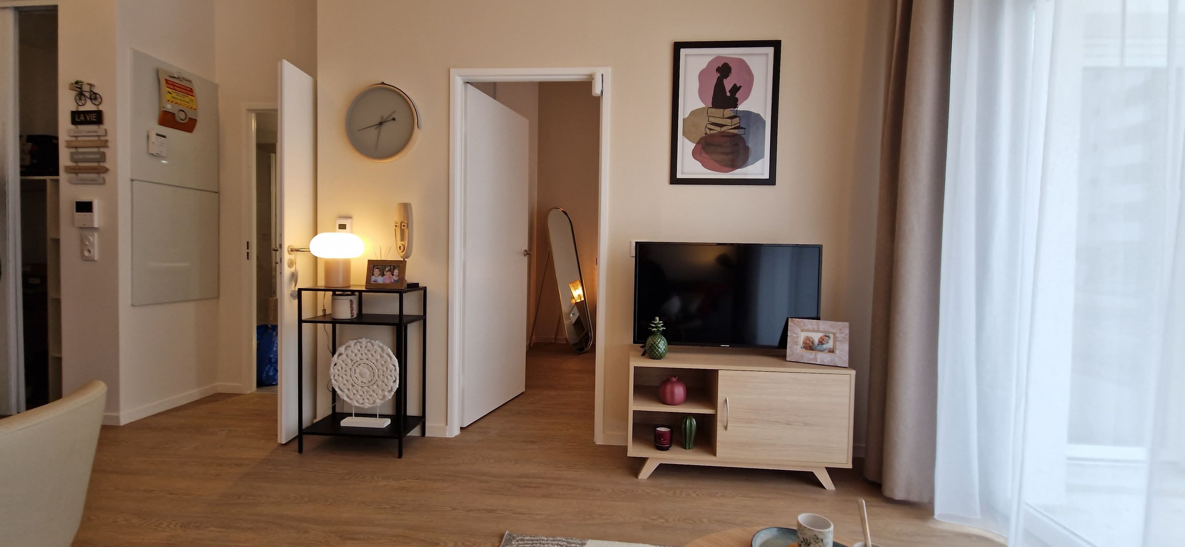 A living room with a television, a framed artwork, a clock, and a door leading to another room.
