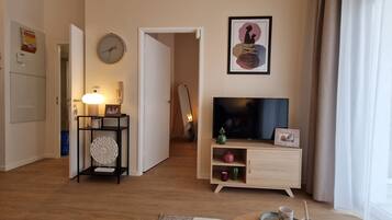 A living room with a television, a framed artwork, a clock, and a door leading to another room.