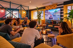 A group of people playing video games in a room with yellow furniture, a large screen, and a blue play structure.