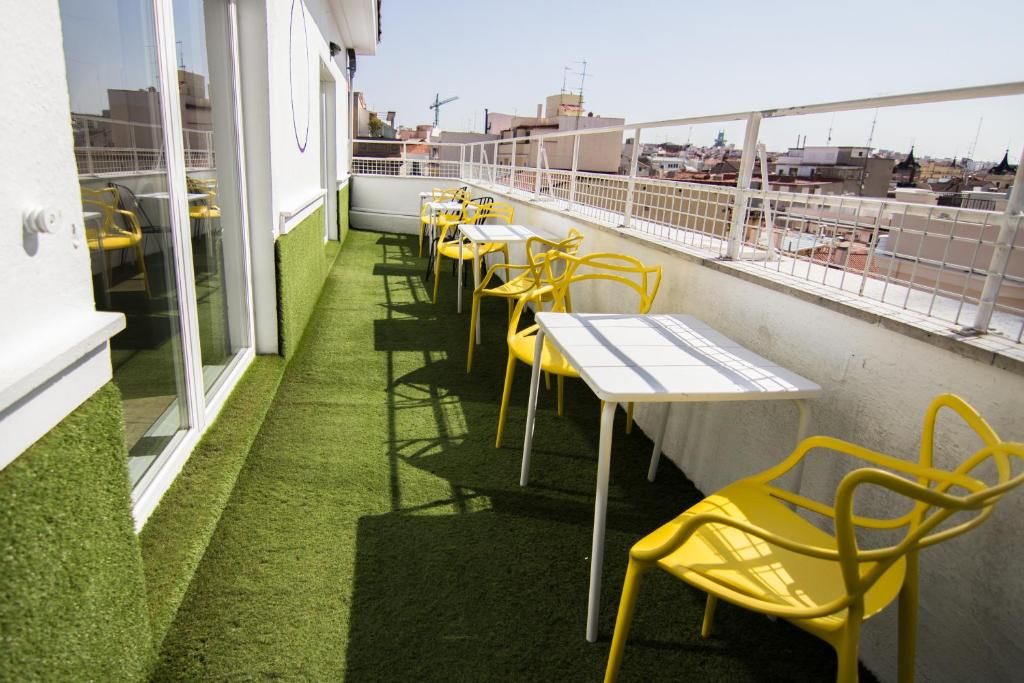 Una terraza en la azotea con sillas y mesas amarillas, una barandilla blanca y vistas de la ciudad.