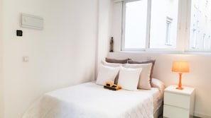 A bedroom with a bed, pillows, a nightstand, a lamp, and a window. - Password to Madrid Plaza España (Madrid)