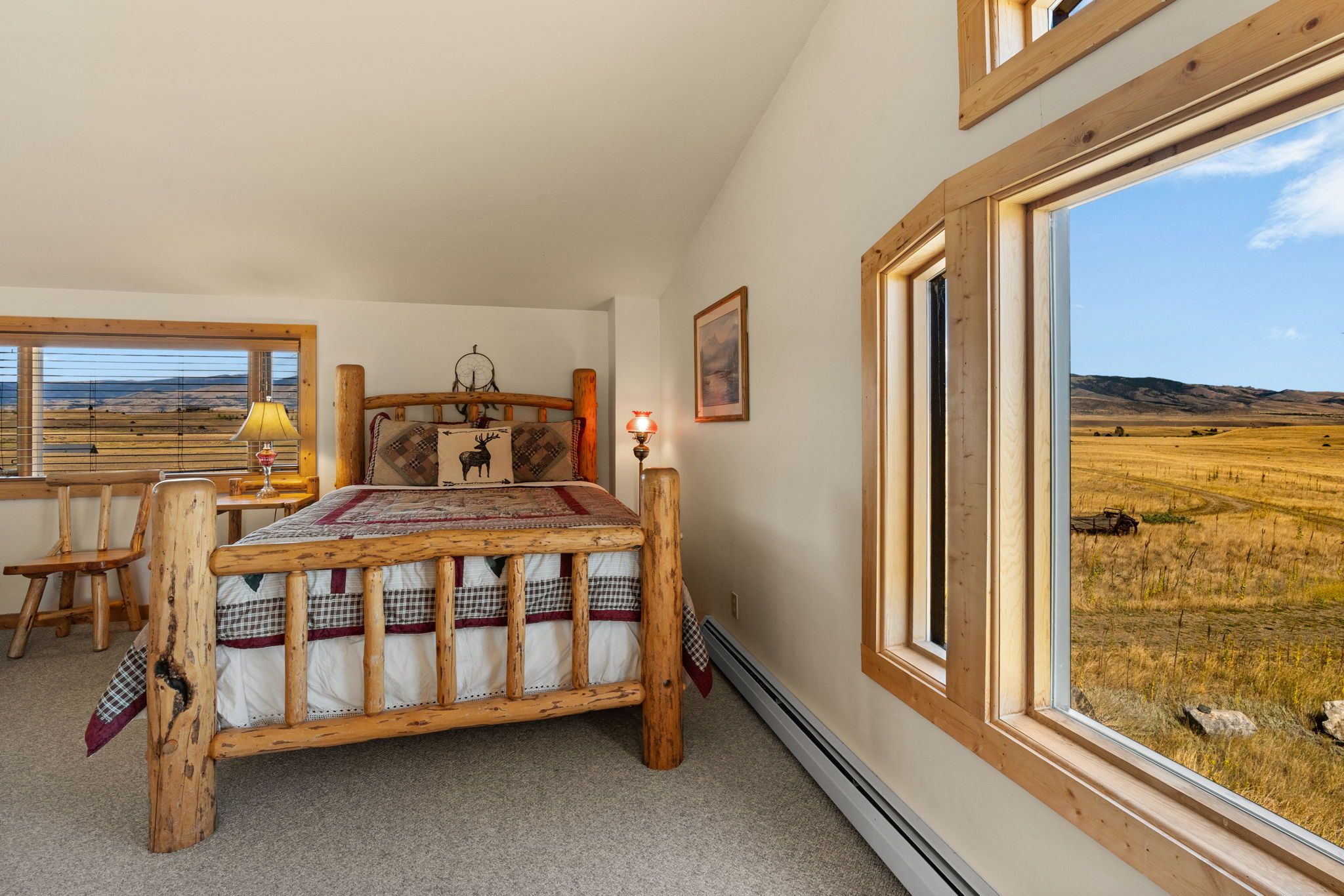A bedroom with a wooden bed, a desk, and a large window with a view of a field.