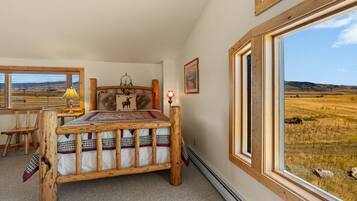 A bedroom with a wooden bed, a desk, and a large window with a view of a field.