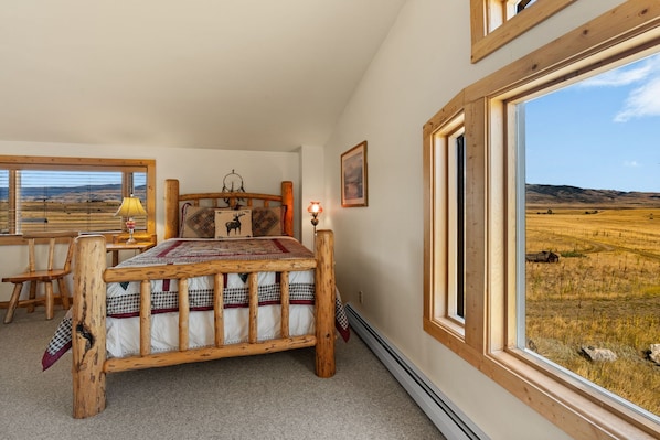 A bedroom with a wooden bed, a desk, and a large window with a view of a field.