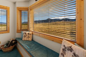 Una habitación con un banco, una cesta y una ventana con persianas de madera que da a un paisaje.