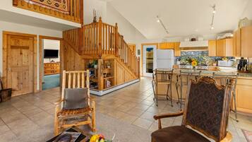 A spacious living area with a wooden staircase, a dining area with a kitchen in the background, and a cozy seating arrangement.