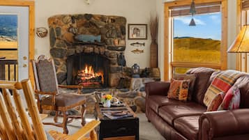 Una sala de estar acogedora con chimenea de piedra, sofá de cuero, mobiliario de madera y vistas al exterior.