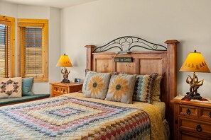 Un dormitorio con cabecera de madera, dos mesitas de noche, una cama con colcha colorida y dos lámparas con base de asta.