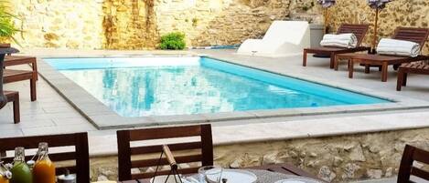 Un área de comedor al aire libre con piscina, paredes de piedra y vegetación.
