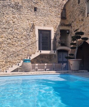 A stone building with a pool, outdoor seating, and a staircase leading to a door.