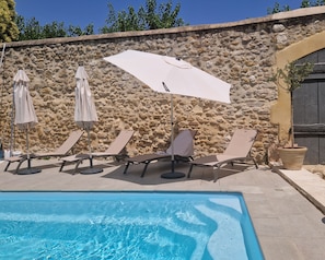 A poolside area with lounge chairs and umbrellas, a stone wall, and a clear blue pool. - Livia's House. An 18th-century village farmhouse between Uzès and Nîmes. (Sauzet)