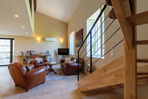 A spacious living area with leather sofas, a wooden staircase, and a large window providing natural light. - Livia's House. An 18th-century village farmhouse between Uzès and Nîmes. (Sauzet)