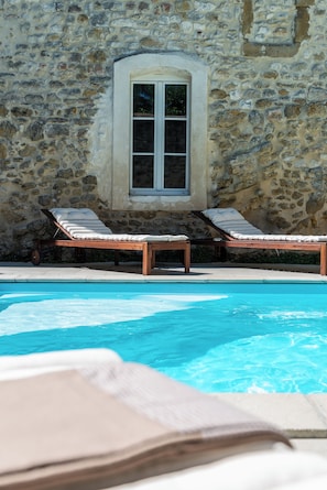 A stone building with a pool, two sun loungers, and a window.