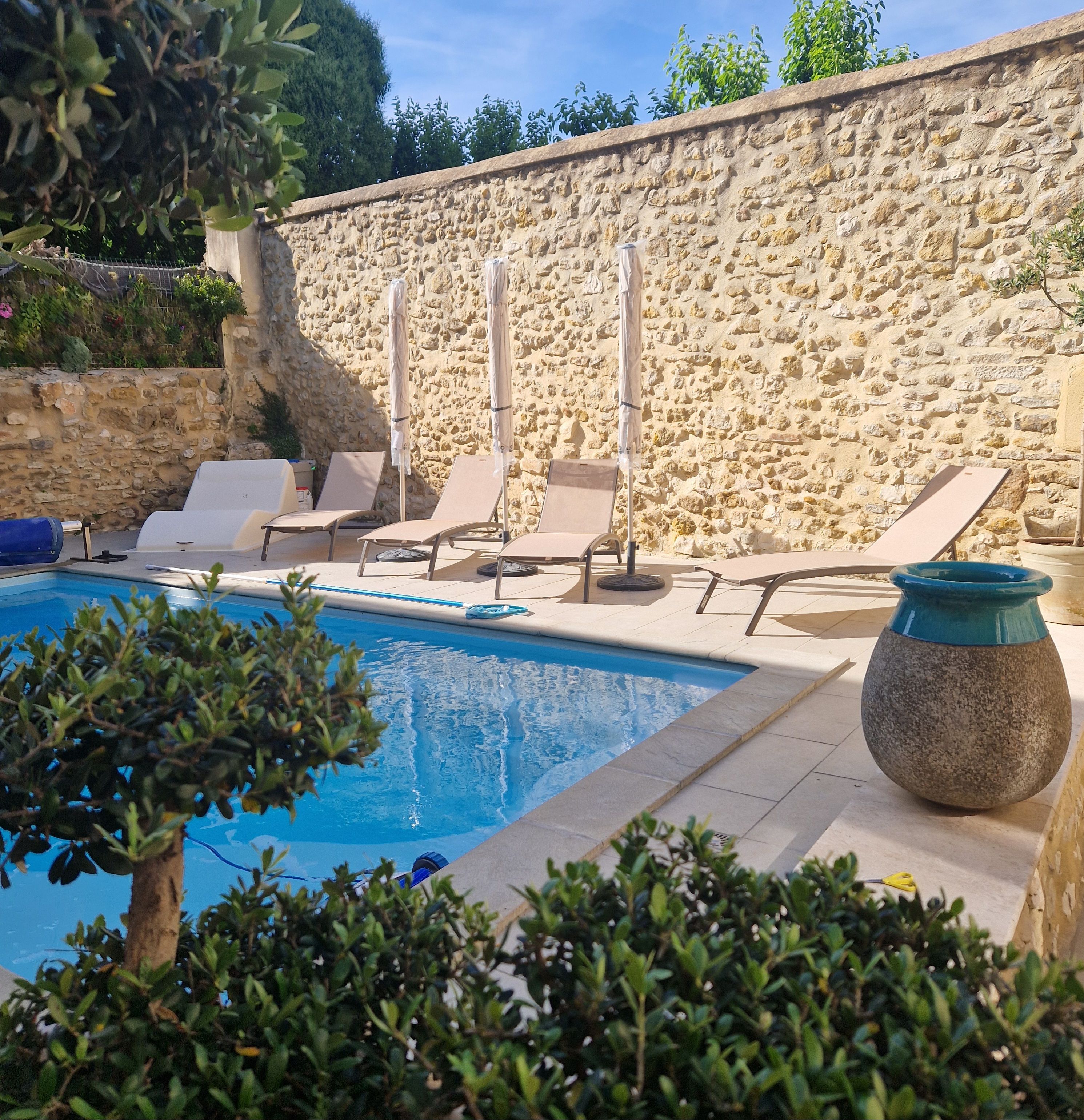 Une piscine avec des chaises longues et un mur en pierre.