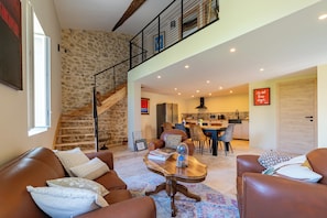 A spacious living area with a stone wall, a wooden staircase, a dining area, and a kitchen. - Livia's House. An 18th-century village farmhouse between Uzès and Nîmes. (Sauzet)