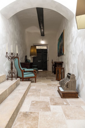 A hallway with a stone floor, a wooden chair, a candelabra, and a vintage camera.