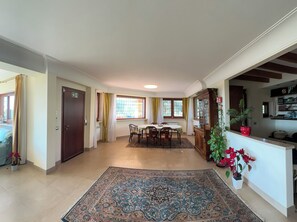 Amplia sala de estar con mesa de comedor, sillas, un tapete grande y un mueble con puertas de vidrio.