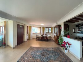 Amplia sala de estar con mesa de comedor, sillas, un tapete grande y un mueble con puertas de vidrio.