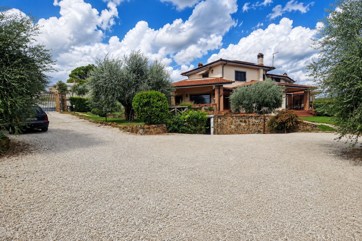 Una casa de dos pisos con entrada de grava, rodeada de árboles y arbustos.