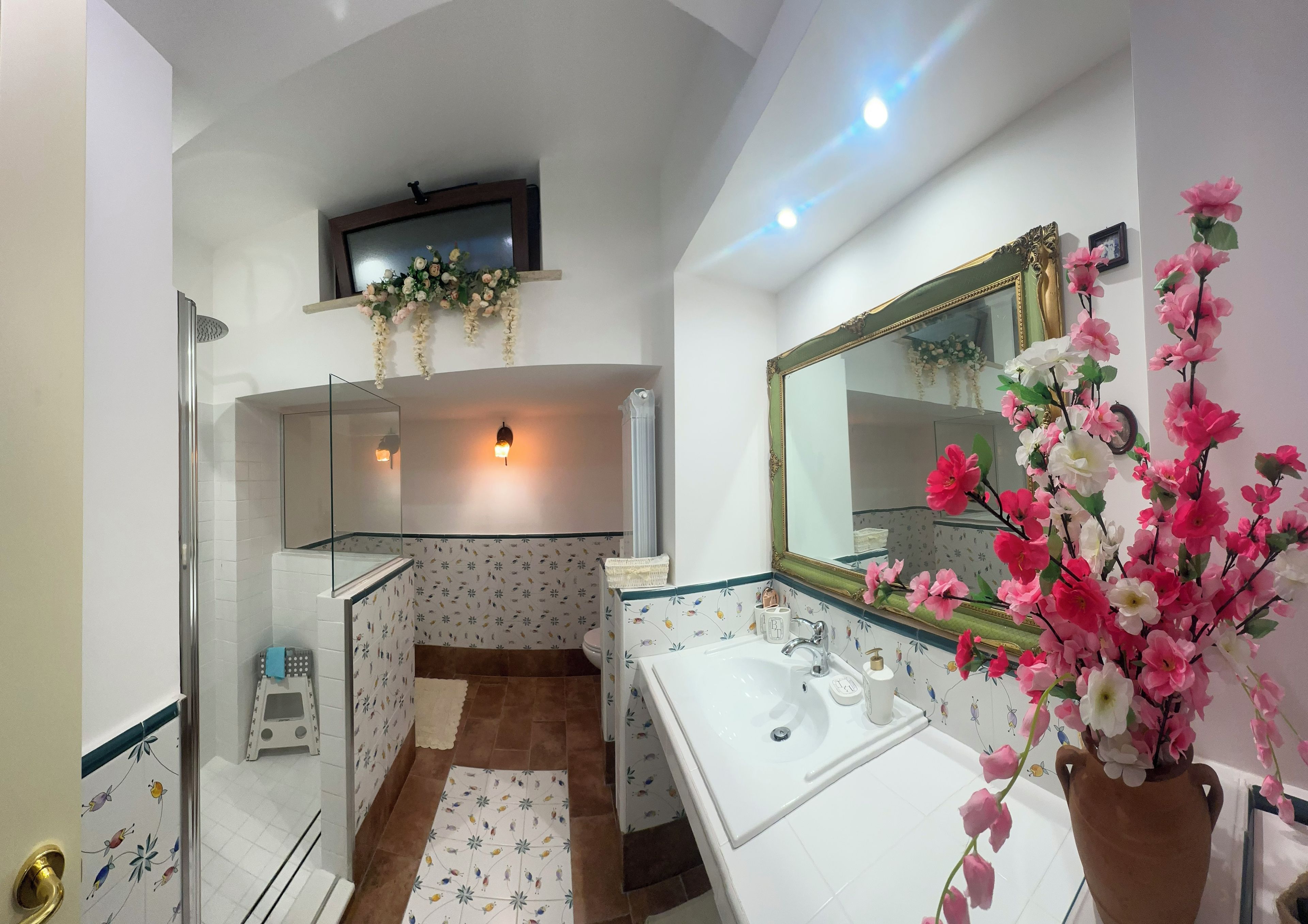 Un baño con ducha, lavabo, espejo y televisor de pared.