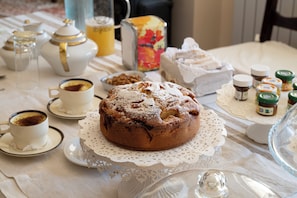 Una mesa servida con un pastel, teteras, tazas y frascos de mermelada.