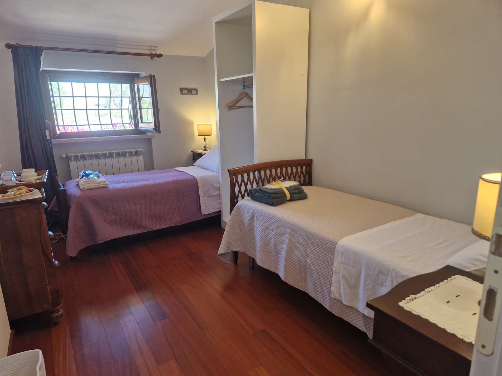 Una habitación con dos camas individuales, un aparador de madera, un radiador y una ventana con cortinas.