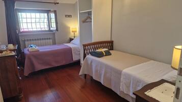 Una habitación con dos camas individuales, un aparador de madera, un radiador y una ventana con cortinas.