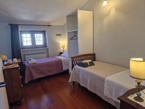 A room with two beds, a radiator, a window with curtains, a table with a lamp, and a wardrobe. - Linda's Retreat B&B (Fiano Romano)