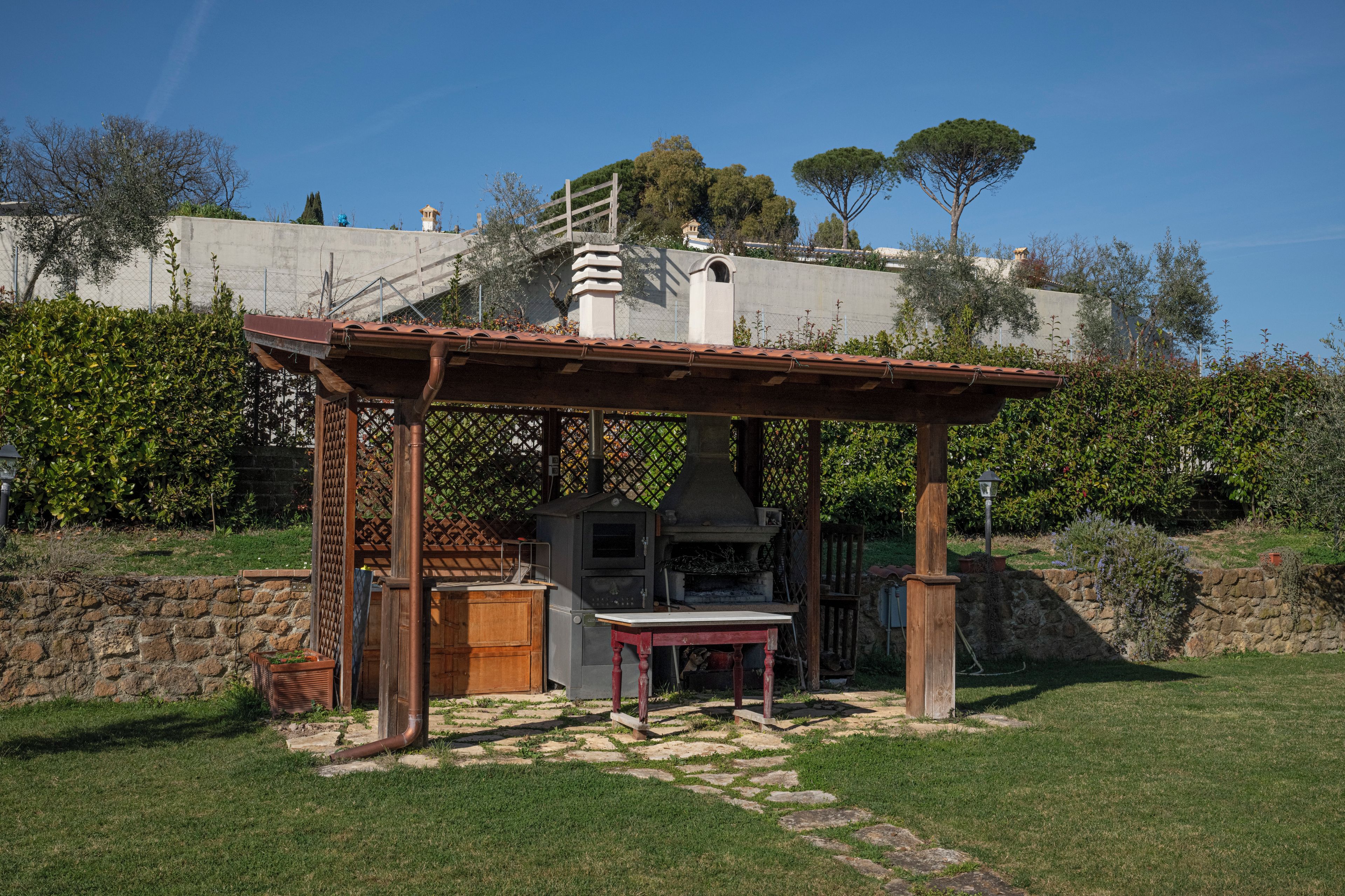 Un área de cocina al aire libre con un pérgola, un camino de piedra y un muro de piedra.