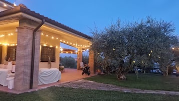 Un'area patio coperta con luci a tendina, una zona relax all'ombra e un albero.