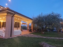 Un patio techado con luces colgantes, una zona de estar cubierta y un árbol.
