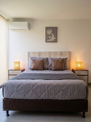 A bedroom with a bed, two bedside lamps, a wall-mounted air conditioner, and a framed artwork. - Residential Park by Domus Travels (San Joaquín)