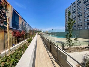 A modern urban walkway with a glass tennis court, adjacent buildings, and a clear sky. - Residential Park by Domus Travels (San Joaquín)