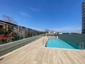 A rooftop swimming pool with a wooden deck, surrounded by buildings and clear skies. - Residential Park by Domus Travels (San Joaquín)