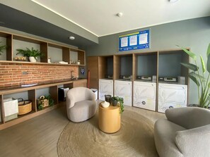A modern waiting area with a brick wall, shelves with plants, a round wooden table, and a seating area with chairs. - Residential Park by Domus Travels (San Joaquín)