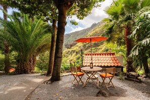 Een terras met een tafel en stoelen, een rode parasol en uitzicht op een bergachtig landschap.