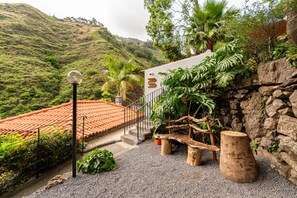 Ein stufenförmiger Garten mit einer Steinsmauer, einer hölzernen Bank und einer Treppe, die zu einem Gebäude mit roten Ziegeldach führt.