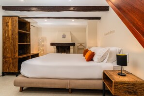 Een slaapkamer met een groot bed, een houten garderobe, een open haard en een kapstok aan de muur.